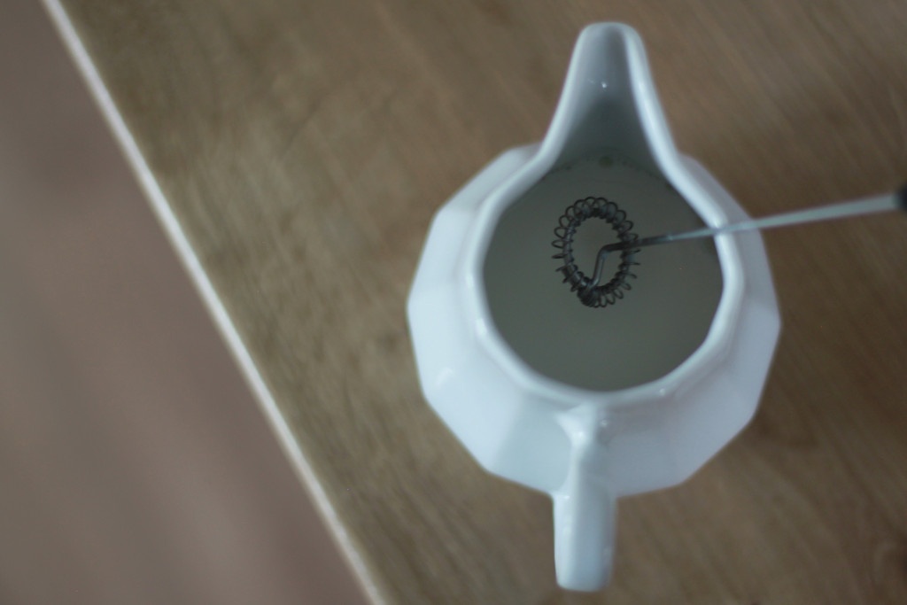 elektrický ruční šlehač mléka v bílé keramické konvičce na mléko
