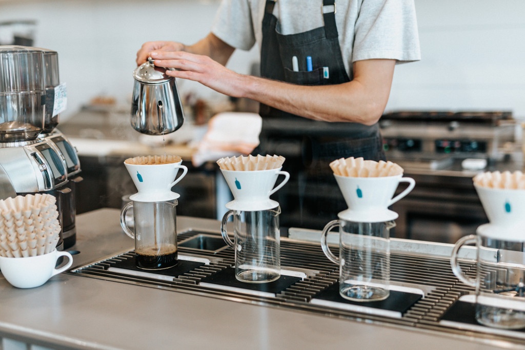 barista připravuje čtyři filtrované kávy formou přípravy v bílých keramických V60