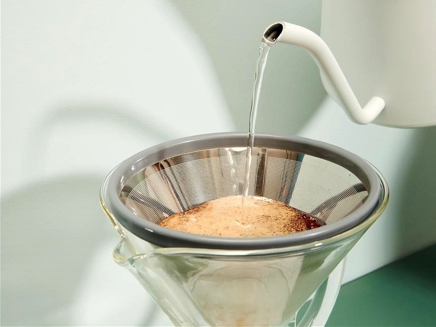 bílá baristická konvice s husím krkem zalévající kávu v kovovém filtru Able