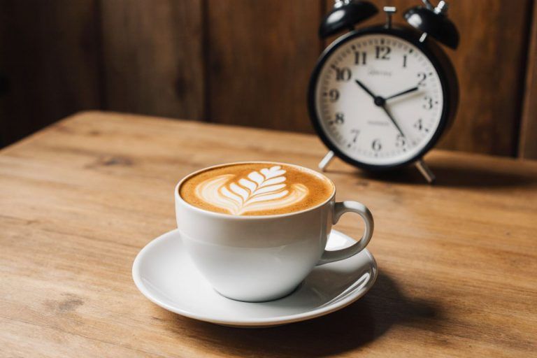 šálek cappuccina s budíkem v pozadí