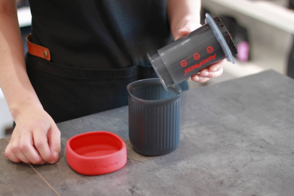 šedý cestovní nástroj na přípravu filtrované kávy AeroPress Go s červeným víčkem