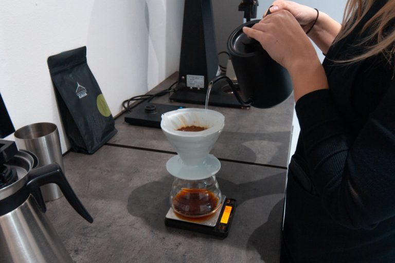 baristka připravuje filtrovanou kávu v bílém dripperu V60